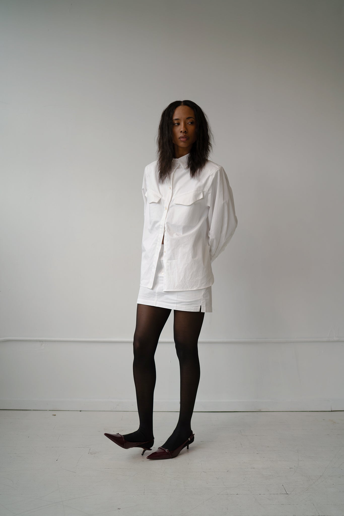 HCTR Oversized Cotton Poplin Button Down in White styled with matching boxer skirt and black tights, full front view